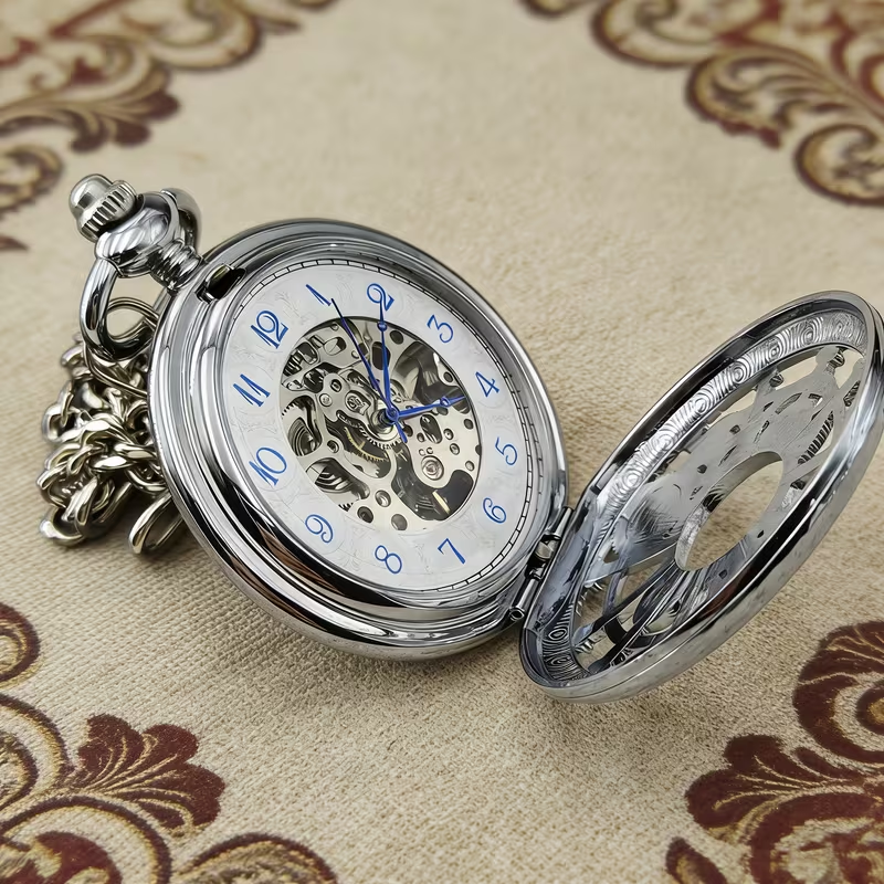 Reloj plateado abierto con números arábigos azules y centro mecánico visible
